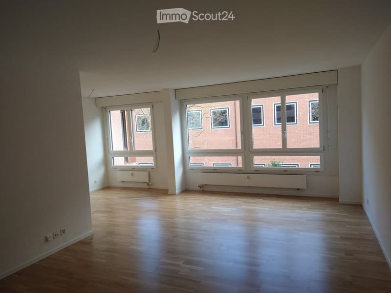 Unfurnished Room. Empty room with white walls, wooden floor, and large windows facing a brick building.