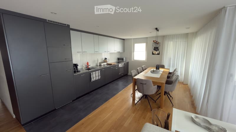 Open-plan kitchen and dining area with modern grey cabinets, a wooden dining table with six chairs, and various kitchen appliances.