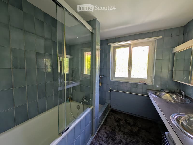 Bathroom. Modern bathroom with blue tiles, a bathtub, a sink, and a mirror. Features a glass-enclosed shower area and a window providing natural light.