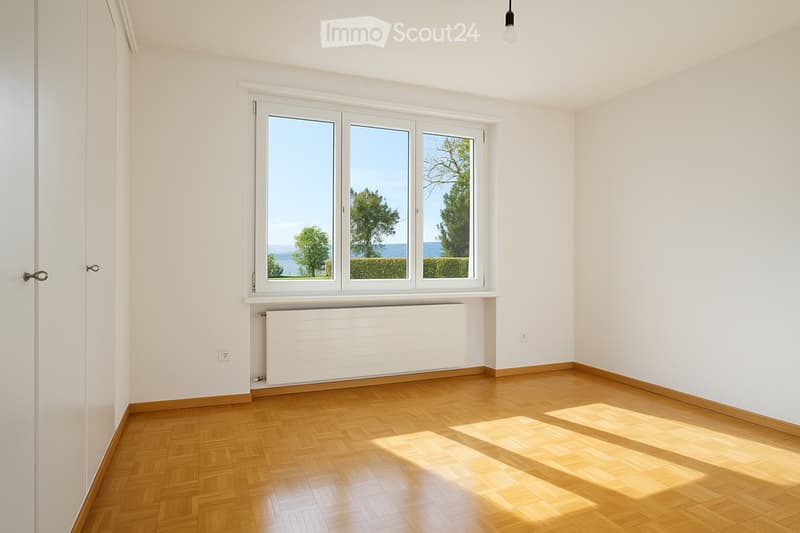 Unfurnished Room. Empty room with wooden flooring, white walls, large window with a view of trees and water, radiator below the window, and a single light fixture on the ceiling.