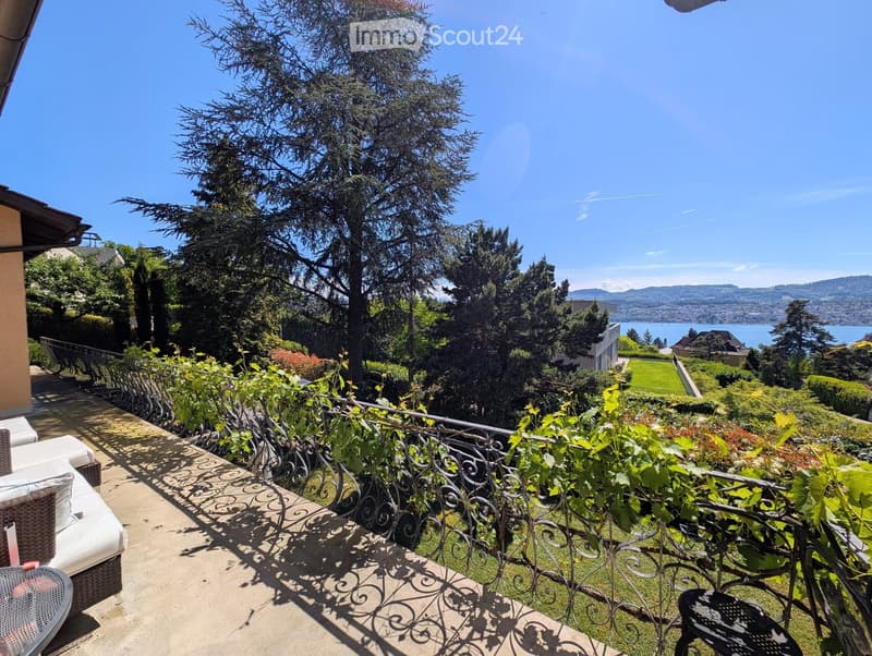Balcony / Terrace. Balcony with a view of a lake and surrounding greenery, featuring a white sofa, a table, and a decorative railing.