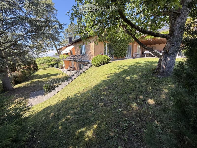 Garden / Outdoor Area. A well-maintained garden with a grassy lawn, trees, and a house with a balcony and patio area.
