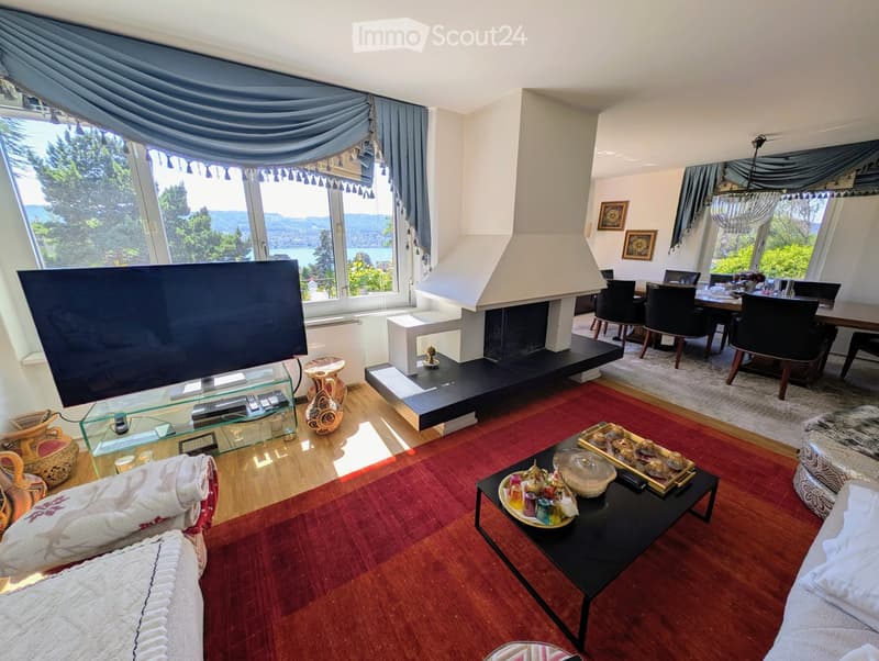 Living Room. Spacious living room with large windows offering scenic views, a fireplace, a sofa, coffee table, and dining area with chairs and table.