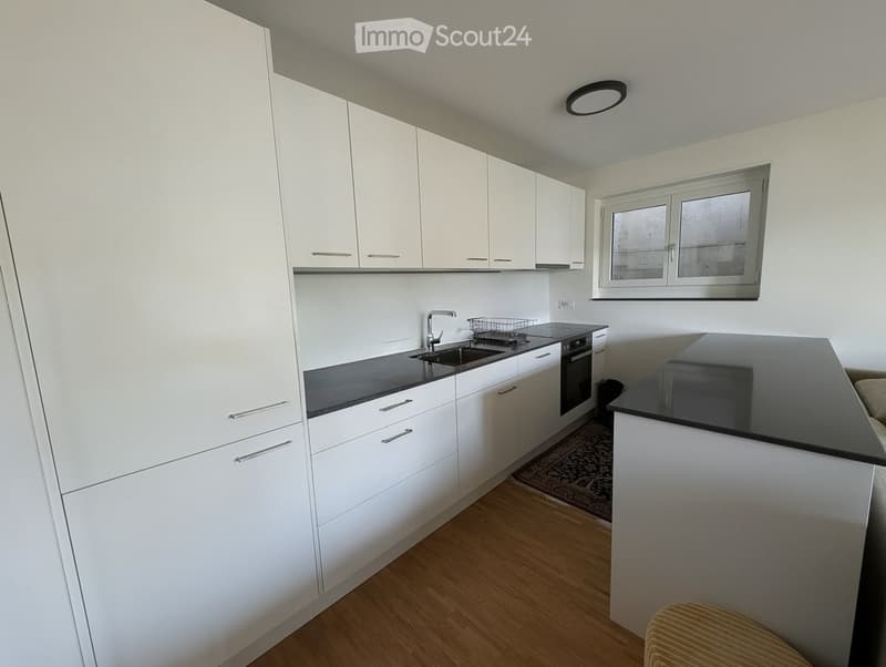 Kitchen. Modern kitchen with white cabinets, black countertops, a sink, and an oven. The space features wooden flooring and a small window above the sink.