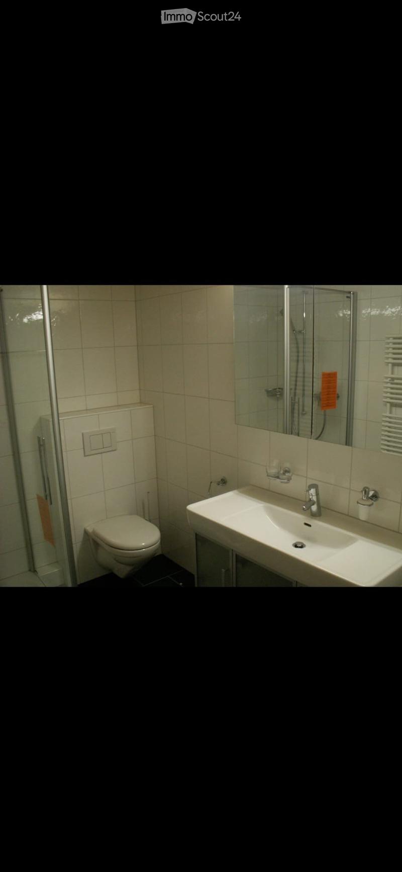 Modern bathroom with white tiles, a toilet, a sink with a modern faucet, a glass-enclosed shower, and a towel rack.