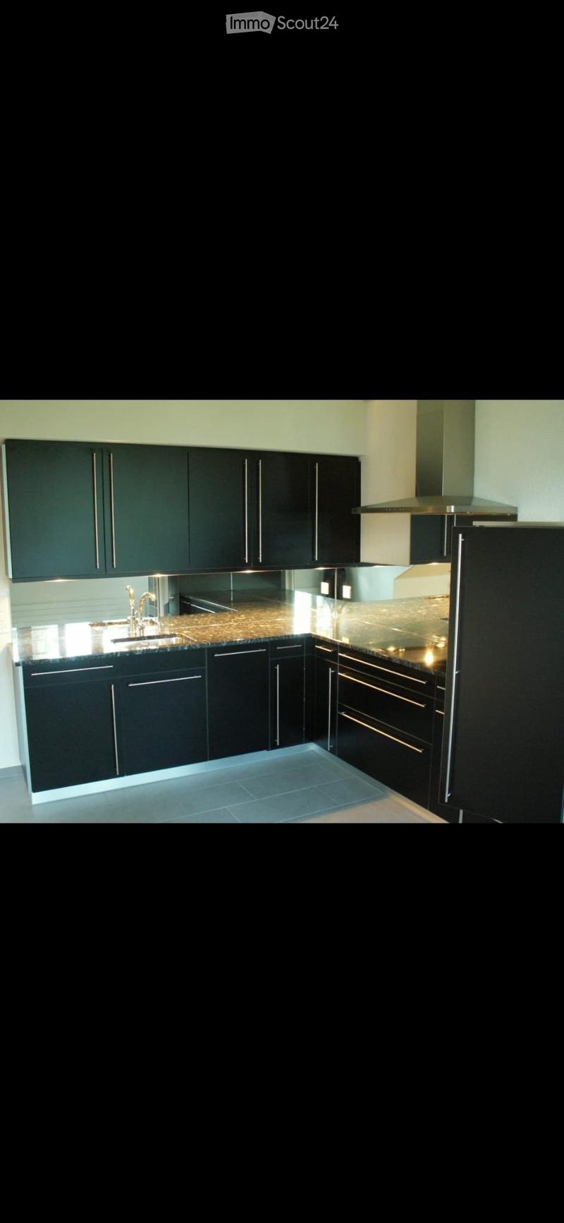 Modern kitchen with black cabinets, granite countertop, stainless steel sink, and range hood.