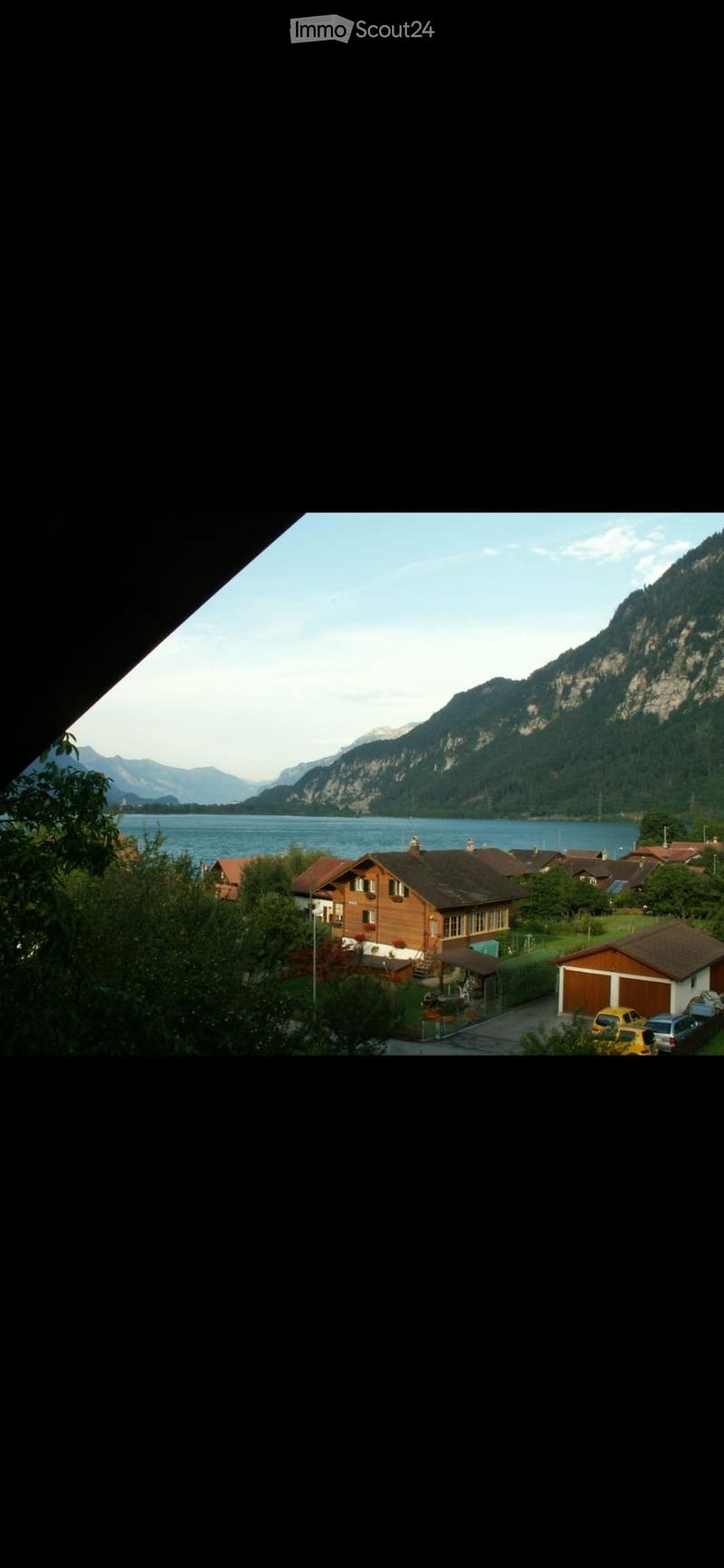 View of a residential area with houses, a lake, and mountains in the background.