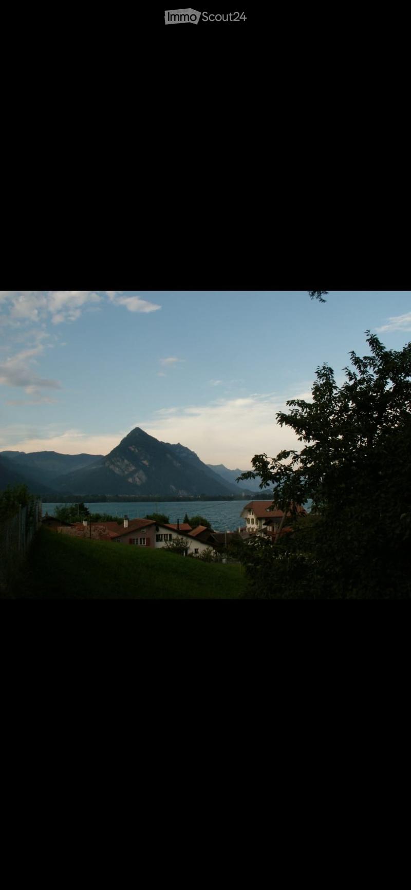 A scenic view of a lake surrounded by mountains, with houses and trees in the foreground.