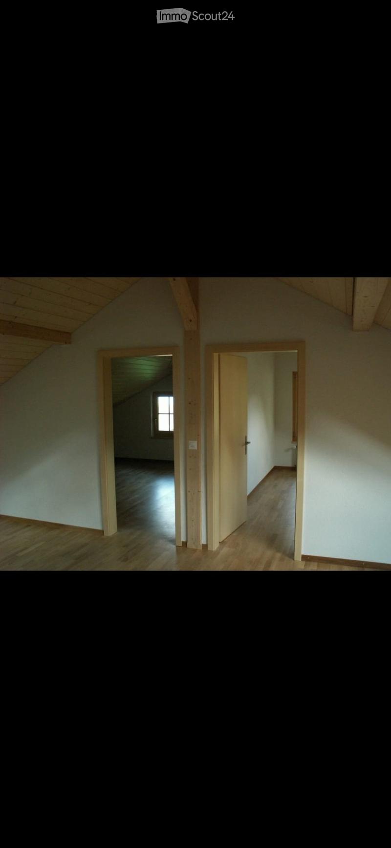 Empty room with wooden flooring, white walls, and exposed wooden beams on the ceiling. Two open doorways lead to adjacent spaces.