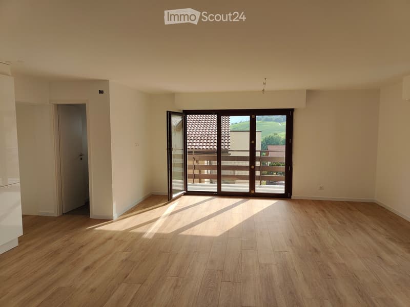 Empty room with wooden flooring, white walls, and large sliding glass doors leading to a balcony with a scenic view.