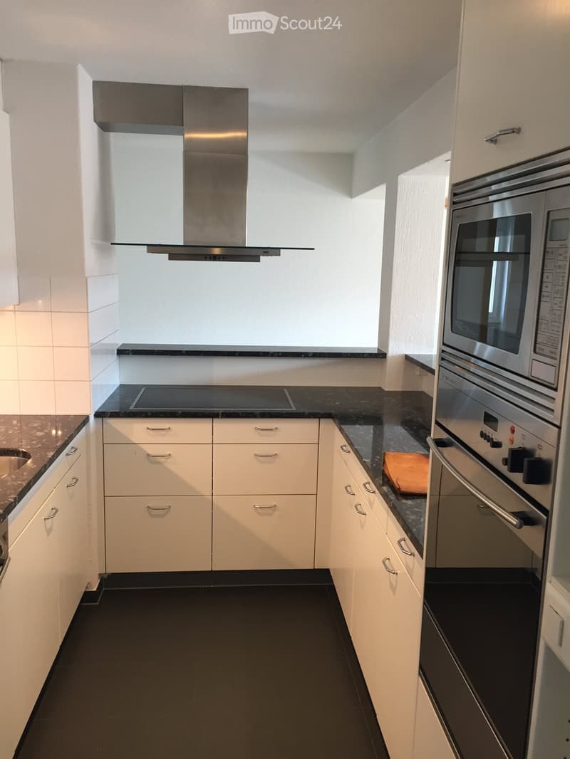 Modern kitchen with white cabinets, black countertops, stainless steel oven, and range hood. Features a sleek design with a black tiled floor.