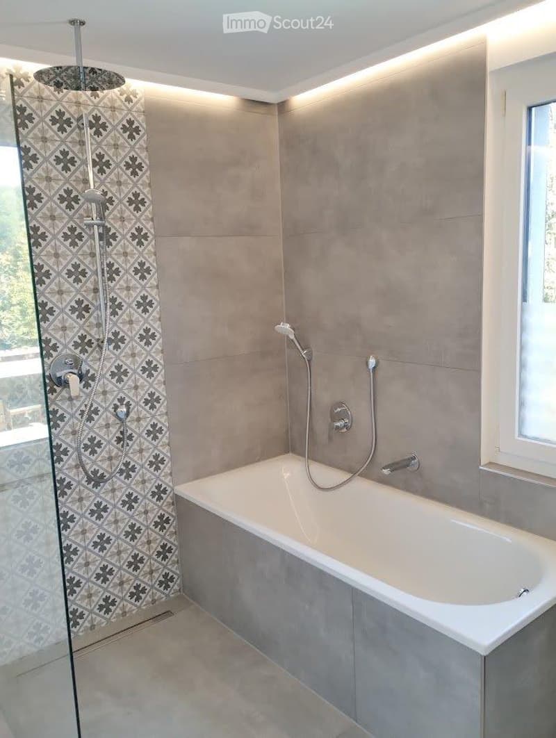 Modern bathroom with a bathtub, glass-enclosed shower, and sleek fixtures. The walls are tiled in a neutral tone with a decorative black and white patterned shower curtain.