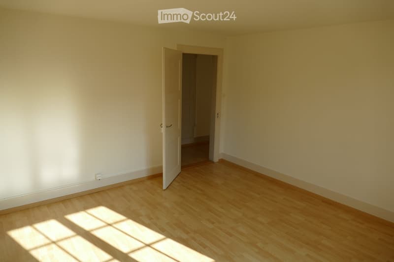 Empty room with light wooden flooring and white walls, featuring an open doorway leading to another space.