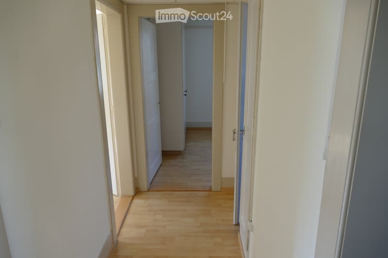 Empty hallway with wooden flooring, white walls, and multiple doors leading to other rooms.