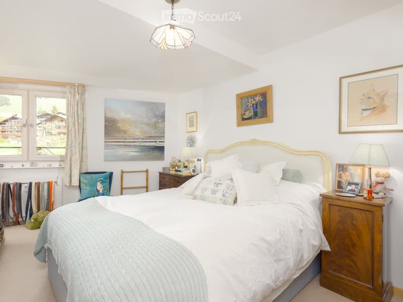 White walls, bed with white bedspread, side tables with lamps, decorative paintings, windows with curtains, lamps