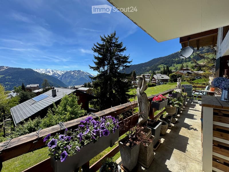 balcony with wooden railings, alpine mountain views, flowerpots, a satellite dish, wooden table, garden statue
