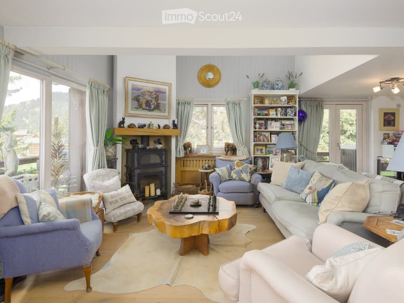 Living room with fireplace, bookshelves, wooden floor, blue couches, center table with chess game, blue chairs, open balcony