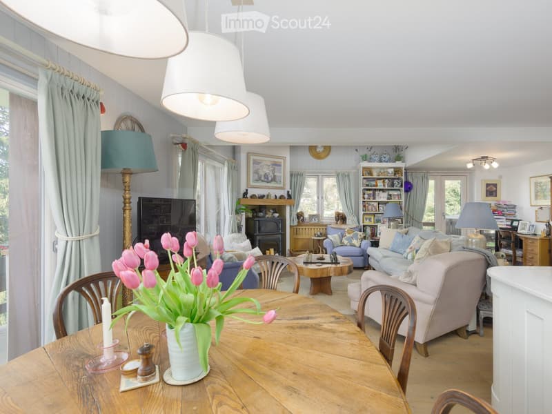 Wooden table with tulips in a vase, white candle, vintage chairs, a lamp, a bookshelf with a fireplace, couch, window, desk, wooden chest, TV.
