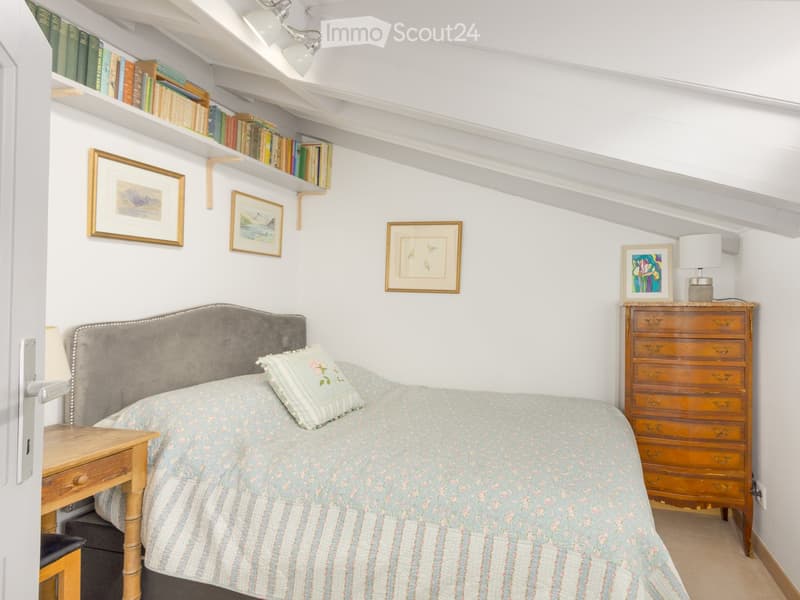 bedroom with bed, nightstand, cabinet, books on shelves, lamps, and picture frames on the wall