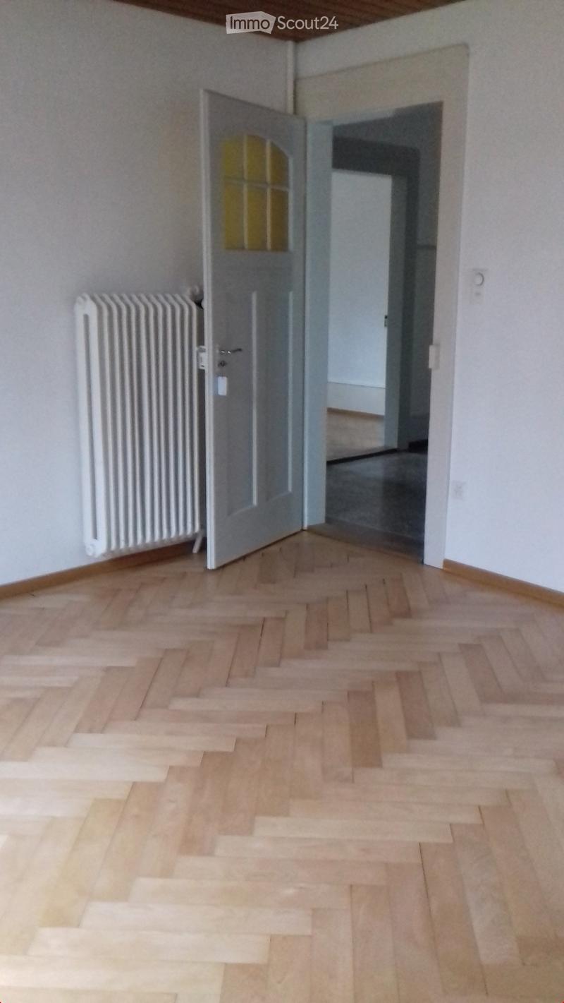Empty hallway with wooden flooring, white radiator, and an open door leading to another room.