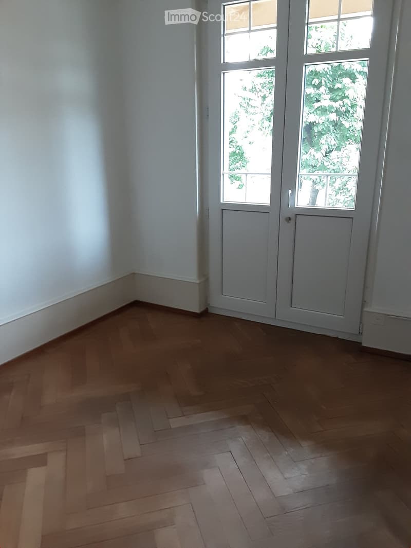 Empty room with light wooden flooring and white walls, featuring a set of double doors with glass panels leading outside.