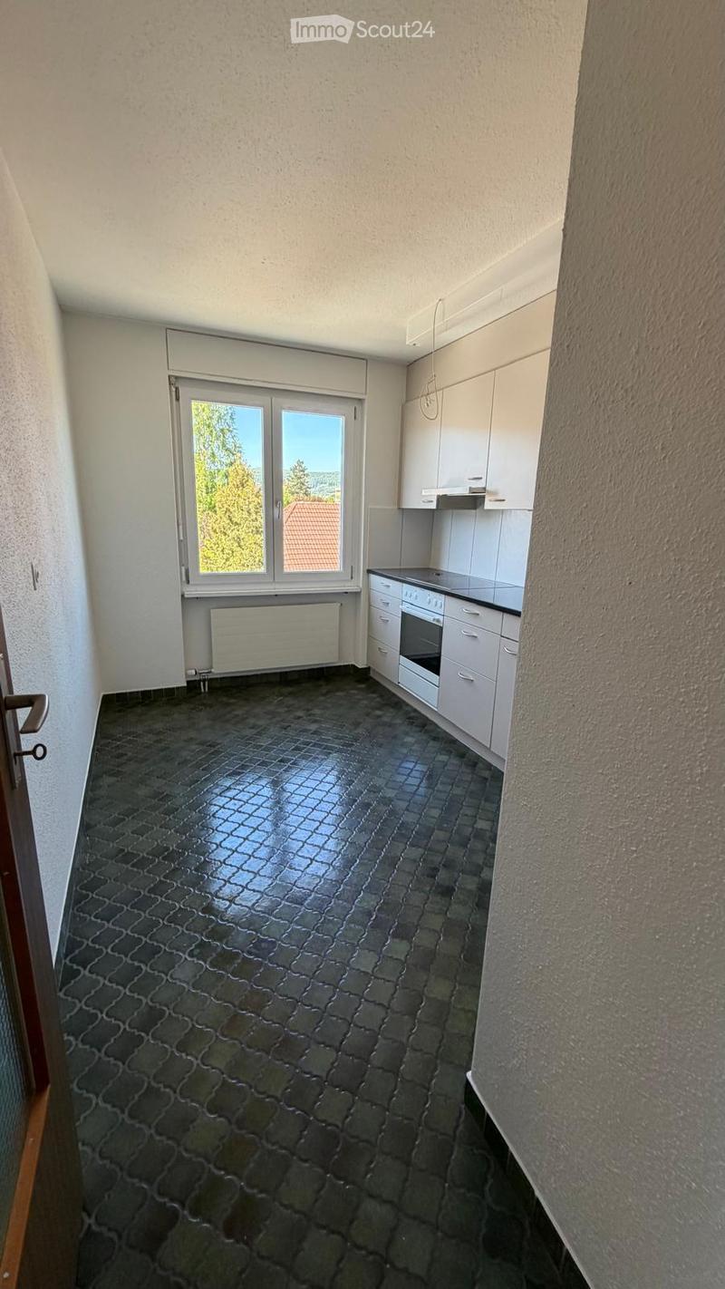 Empty kitchen with white cabinets, a dark tiled floor, and a large window overlooking a green area.
