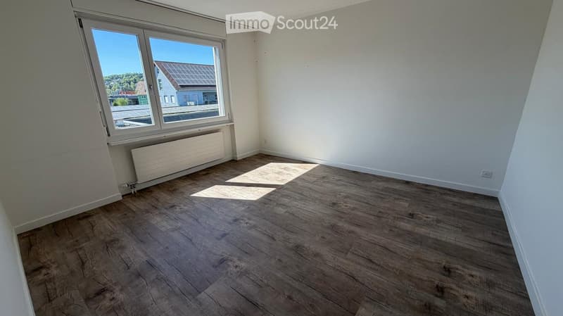 Empty room with wooden flooring, white walls, and a large window with a radiator below it.