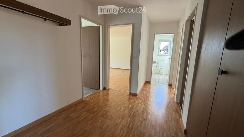 Empty hallway with wooden flooring, white walls, and several doors leading to different rooms, including a visible bathroom.