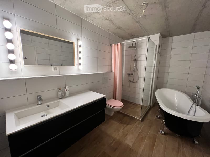 Modern bathroom with a double sink, bathtub, toilet, and walk-in shower. Features include a large mirror with built-in lighting, a glass shower enclosure, and a sleek black vanity.
