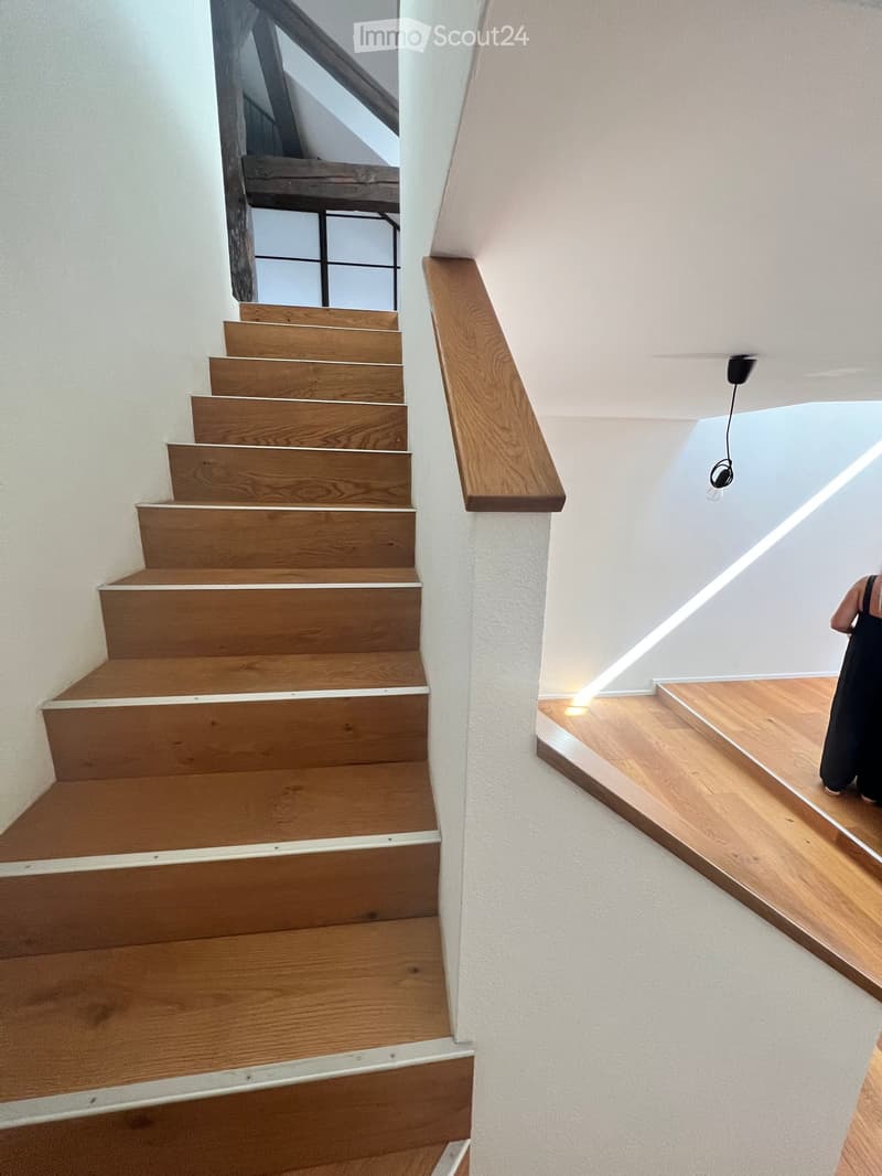 Wooden staircase with modern design, white walls, and built-in lighting along the wall.