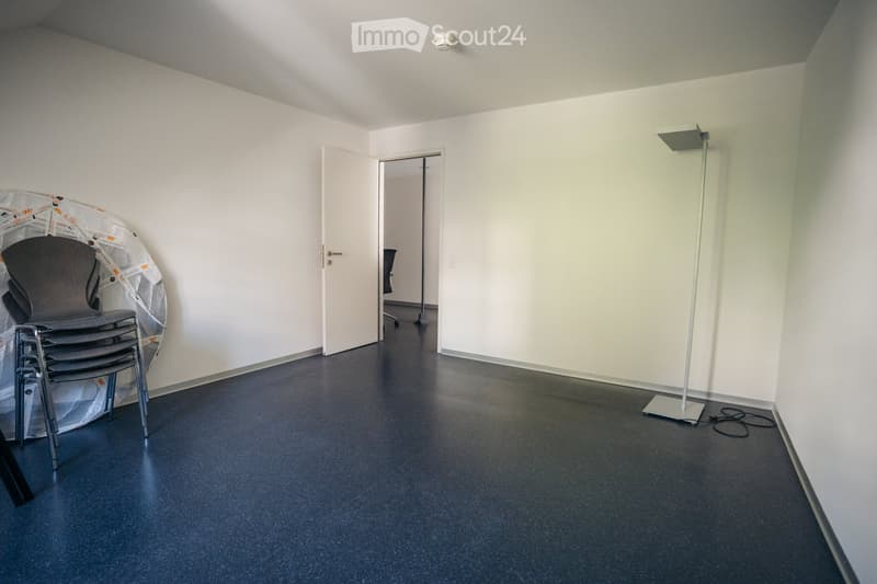 Empty room with white walls, dark flooring, a stack of chairs, and a floor lamp near the doorway.
