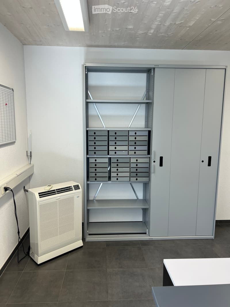 A clean, unfurnished room with a large metal cabinet, air conditioner, and a small table.