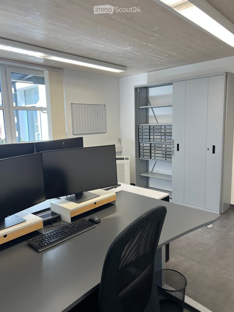 Modern office space with a large desk, computer setup, ergonomic chair, and white cabinet with mail slots.