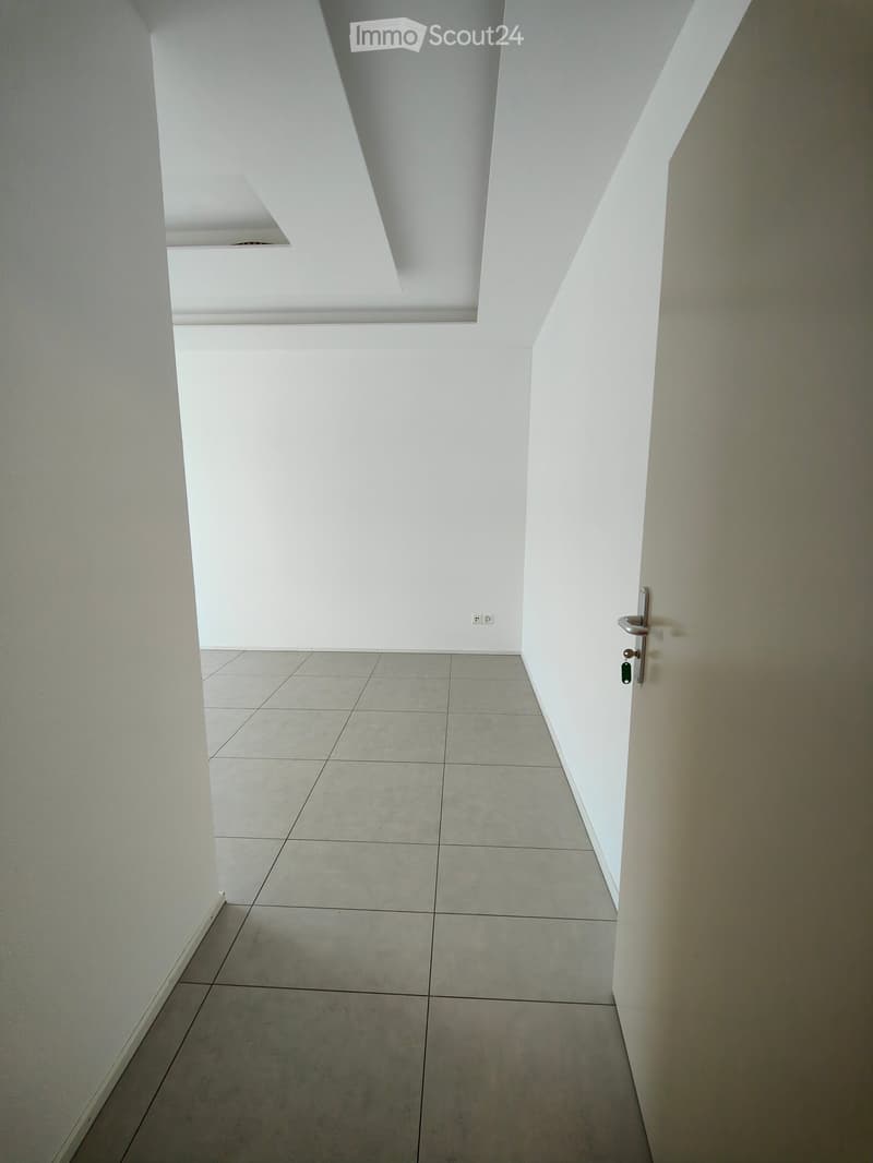 A clean, modern hallway with white walls, tiled floor, and a door on the right side.