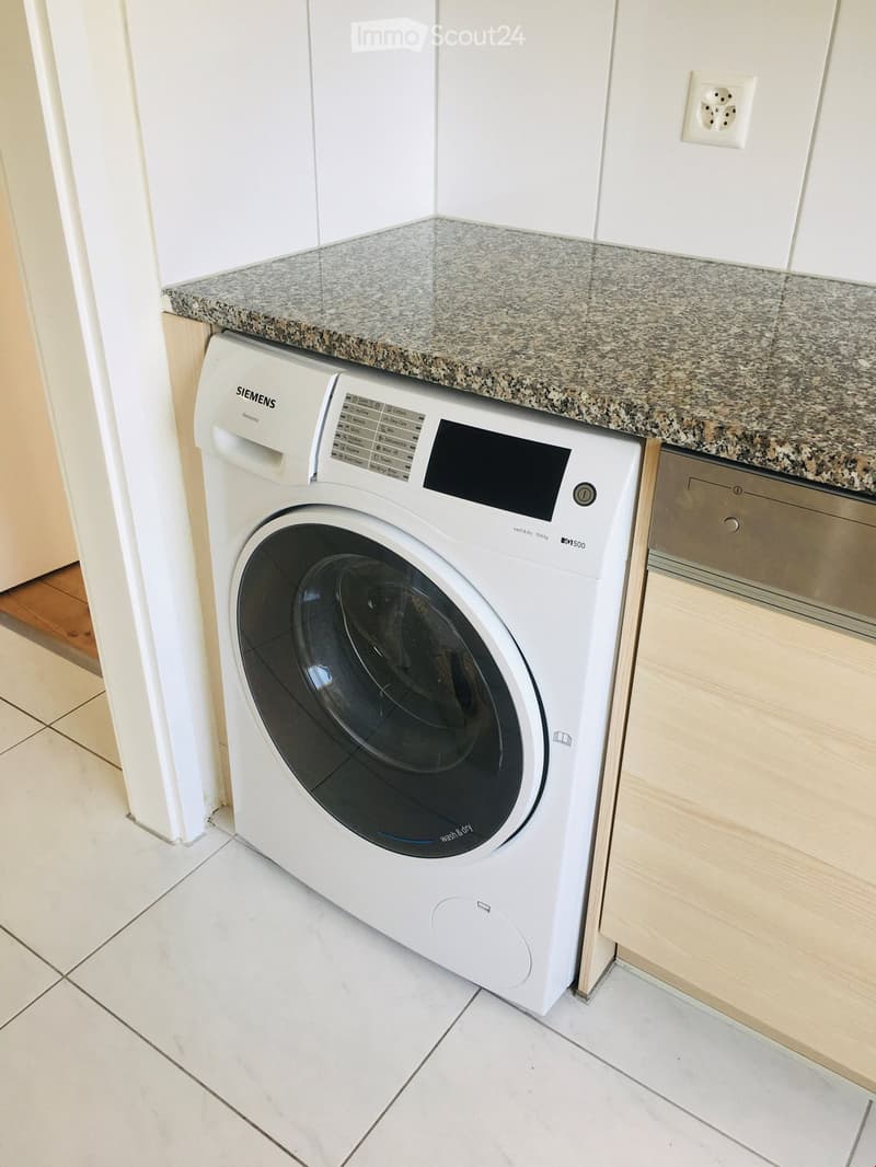 White Siemens washing machine, granite countertop, white tiled floor, white wall, wooden cabinet