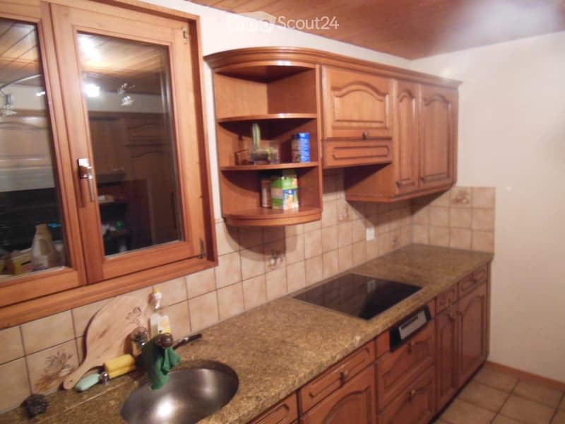 The kitchen features wooden cabinets, granite countertops, a sink with a faucet, and a built-in oven. Shelves hold various items, and a window provides natural light.
