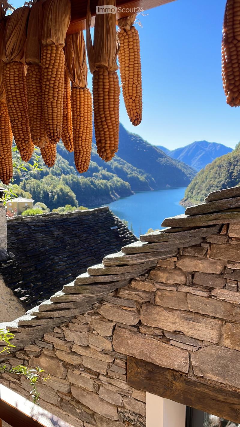 Stone wall with hanging corn cobs, overlooking a scenic lake and mountain landscape.