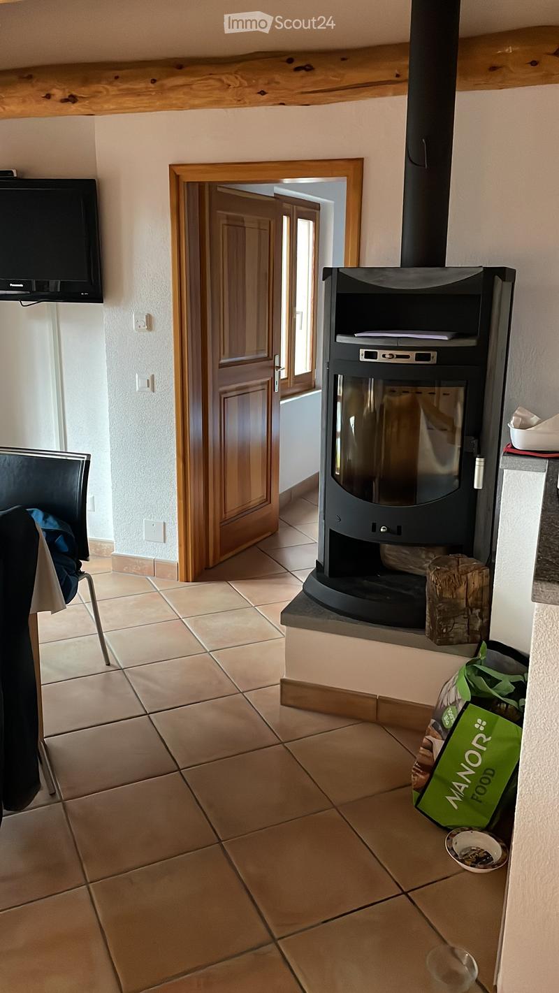 A tiled room with a modern fireplace, a chair, and a screen mounted on the wall. A door leads to another room.