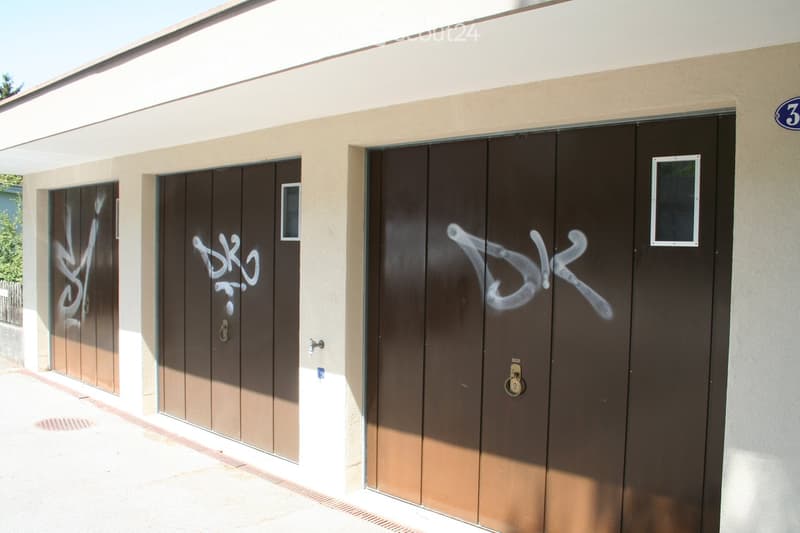 Exterior view of a building with three large garage doors, beige walls, and graffiti on the doors.