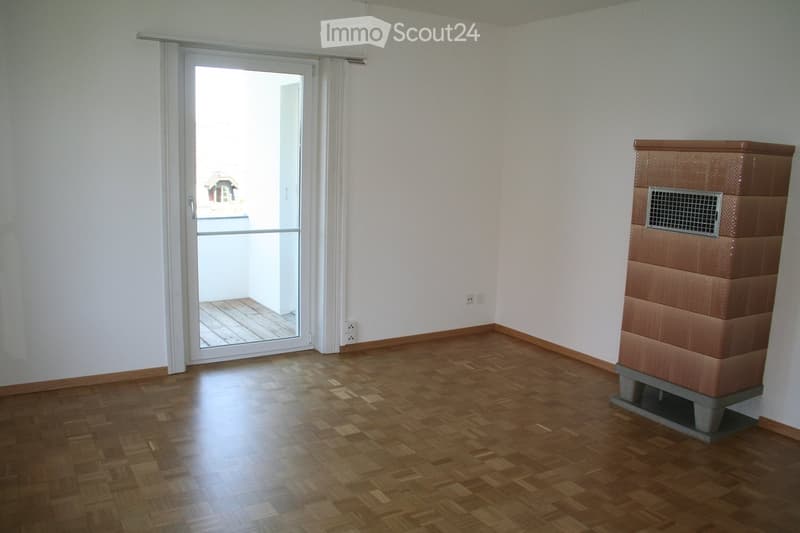 Empty room with wooden flooring, white walls, a sliding glass door leading to a balcony, and a built-in heating unit.