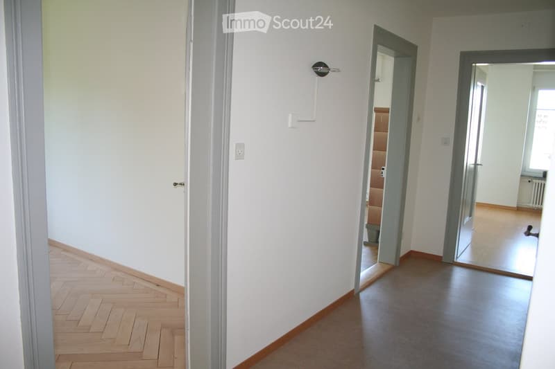 Empty hallway with light-colored walls, wooden flooring, and two open doors leading to other rooms.