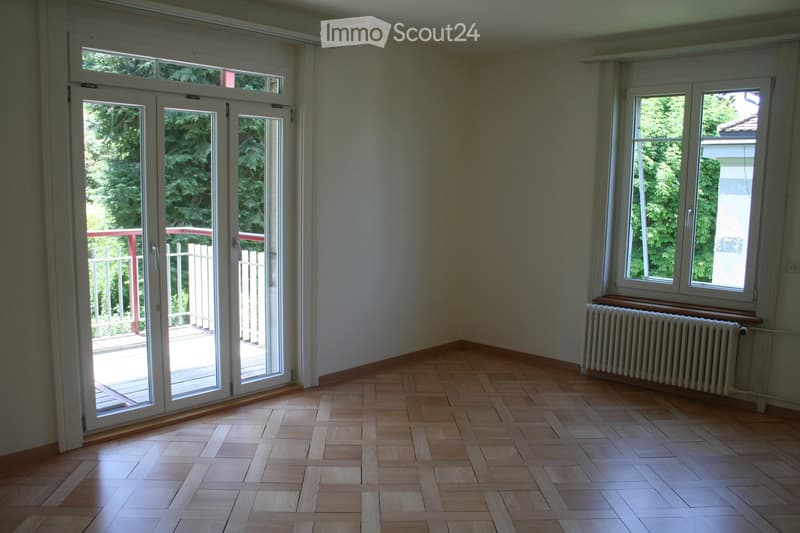 Empty room with wooden flooring, large windows, and a sliding glass door leading to a balcony.