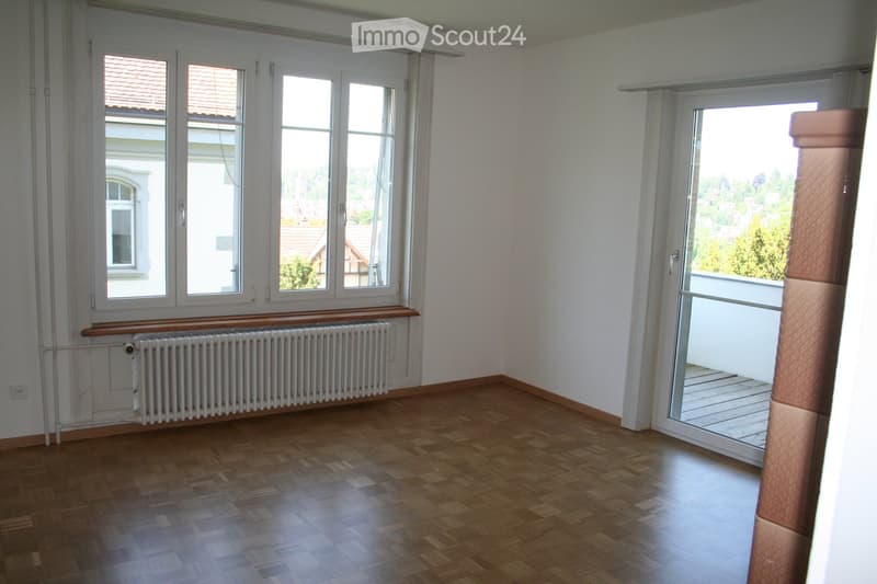 Empty room with wooden flooring, large windows, radiator, and sliding glass door leading to a balcony.