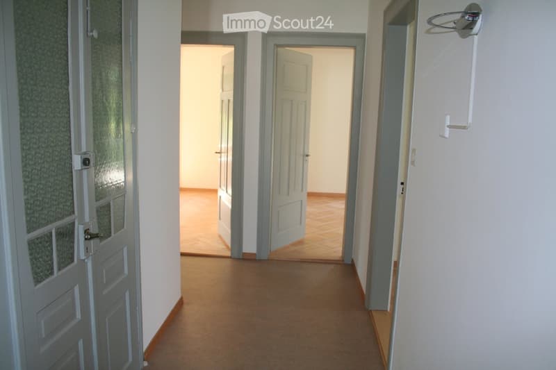 Empty hallway with beige carpeted floor, white walls, and several doors leading to other rooms.