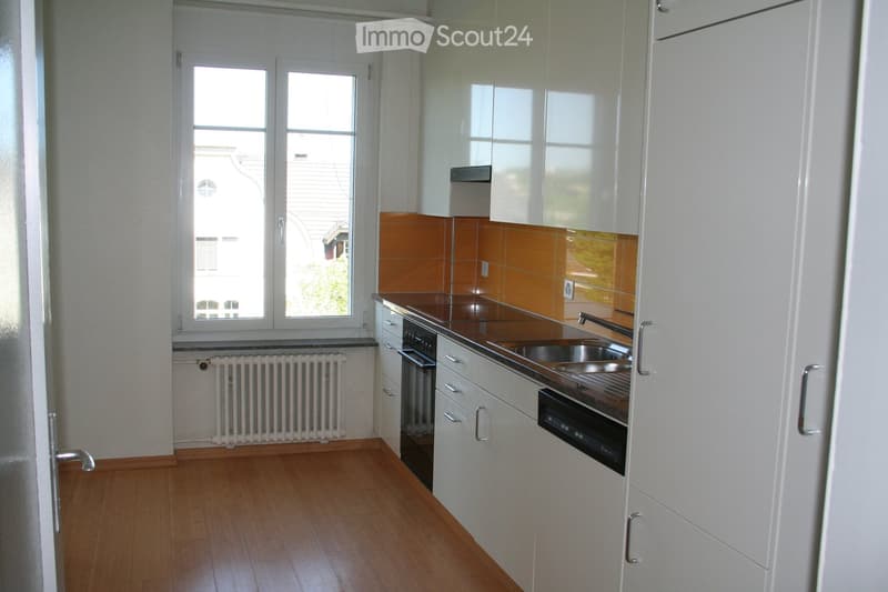 Modern kitchen with white cabinets, dark brown countertop, stainless steel sink, and built-in oven. Features a window with a view of the street and a radiator below.