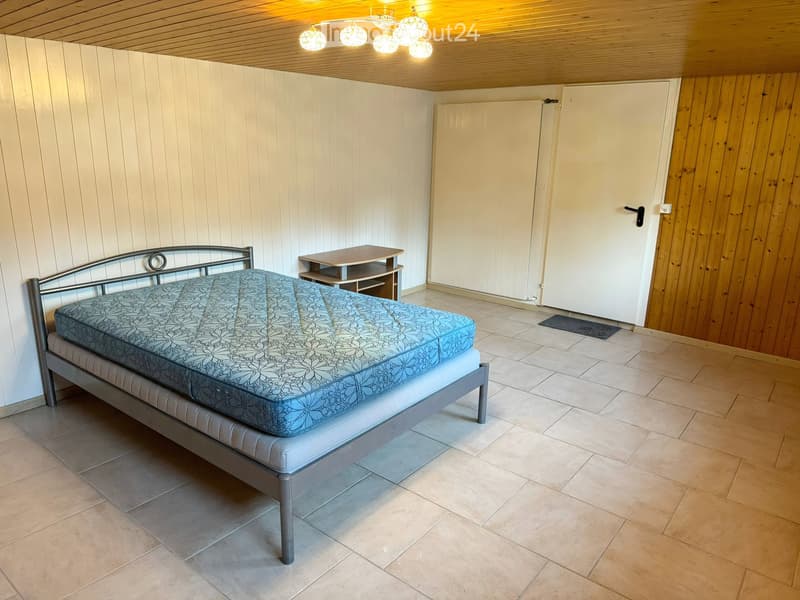 Bedroom with tiled floor, wooden walls, a metal-framed bed with a blue patterned mattress, and a small nightstand.