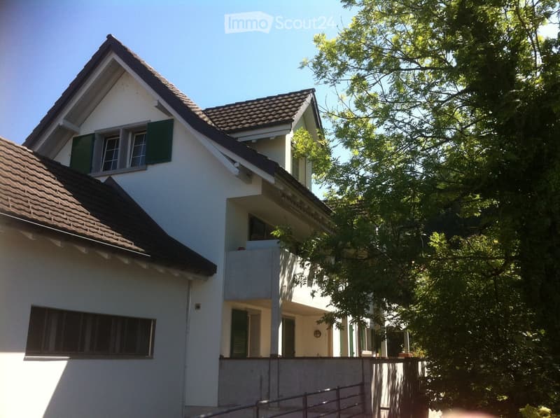 Two-story house with white exterior, brown tiled roof, green shutters, and a small balcony on the upper level.