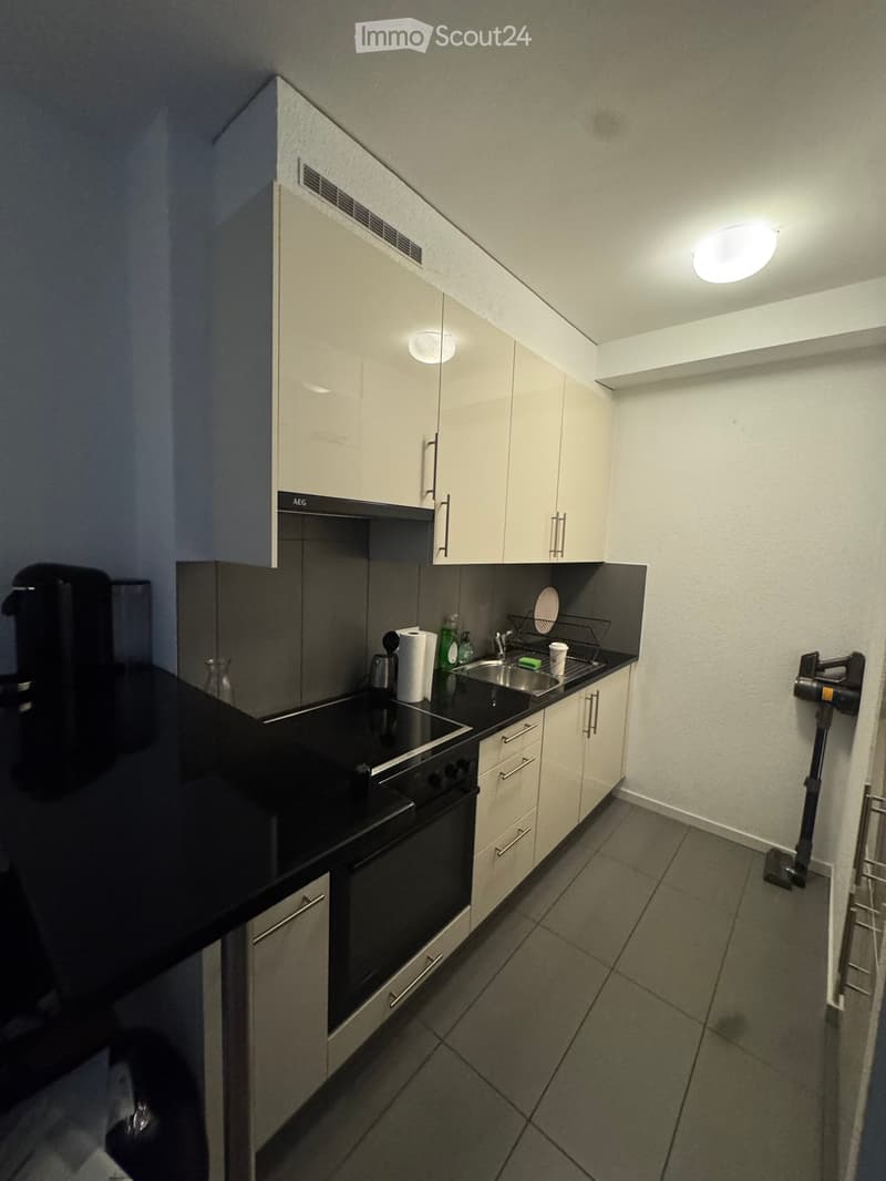 Modern kitchen with white cabinets, black countertops, built-in oven, sink, and various small appliances.