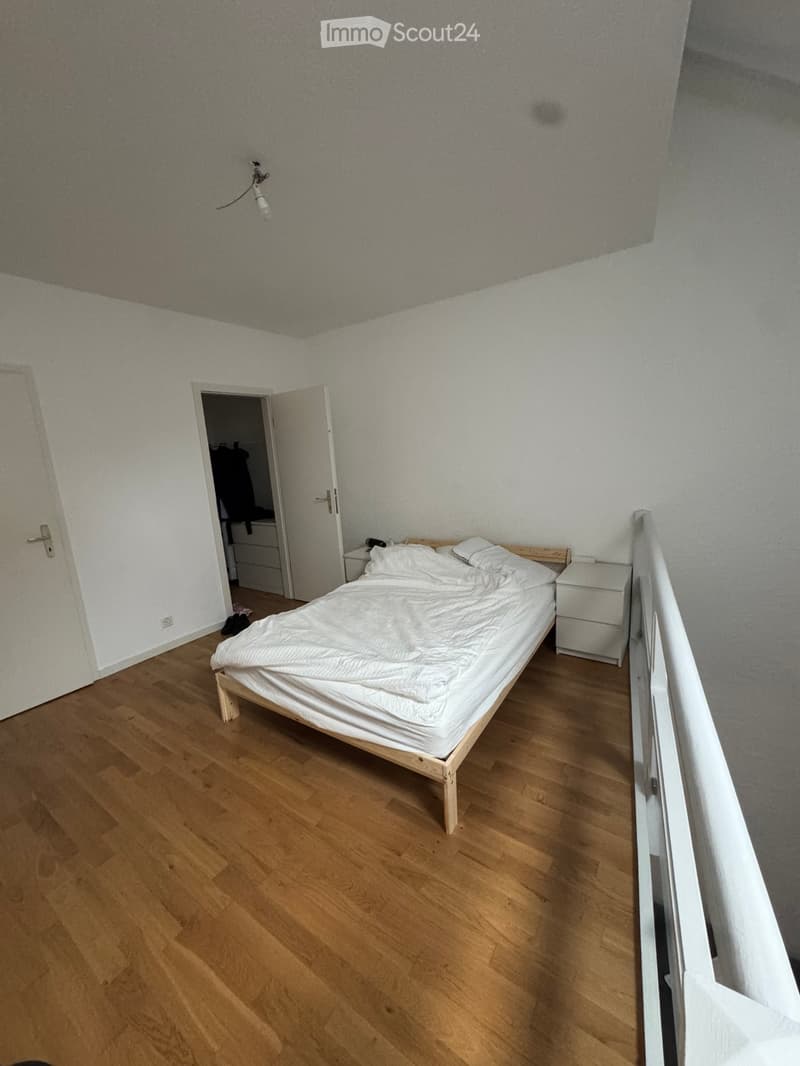 Bedroom with wooden floor, single bed with white bedding, nightstand, and lamp. Open closet door visible in background.