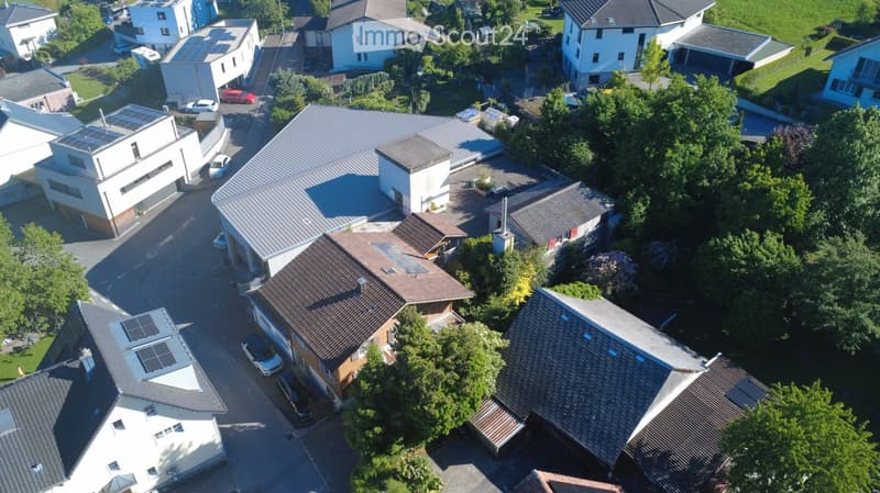 Aerial view of a residential area with multiple houses, solar panels on some roofs, and parked cars in driveways.